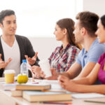 Cheerful students. Four cheerful students talking to each other while sitting at the desk